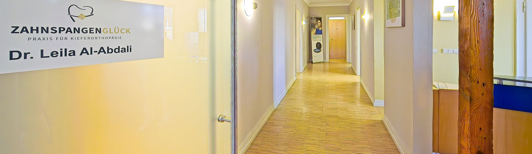 Offene Glastür mit dem Logo von Zahnspangenglück und mit Blick in den Flur der Praxis für Kieferorthopädie in Weinheim